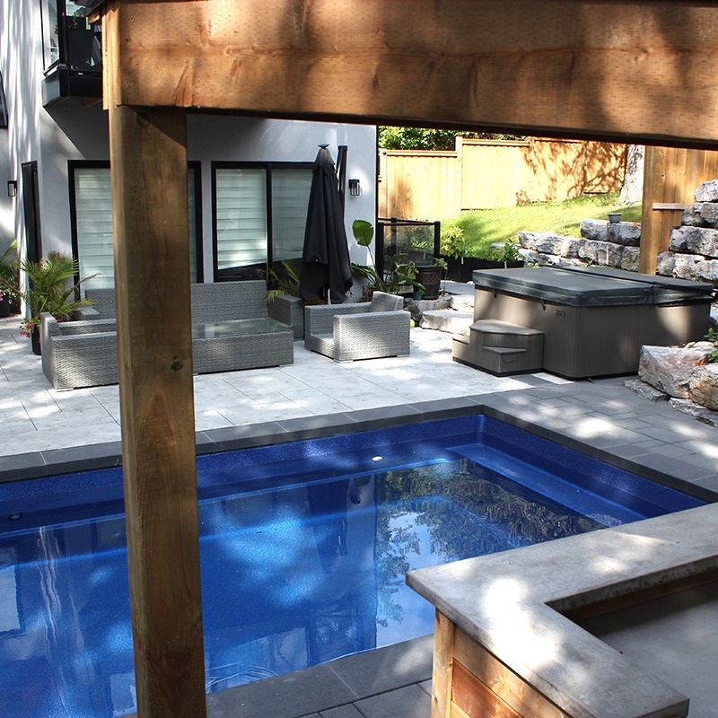 Modern backyard patio featuring a pool, hot tub, and outdoor seating area. The space is surrounded by decking and landscaped greenery.