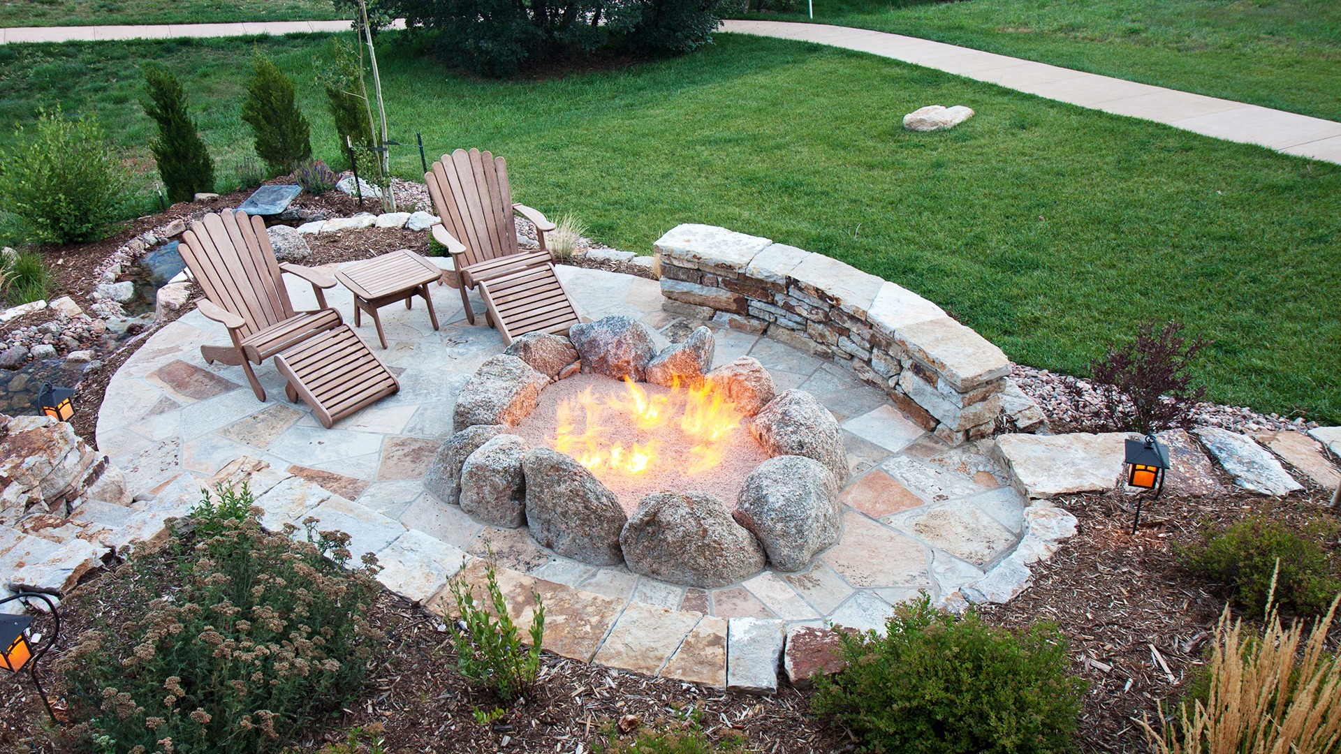 Pool landscaping ideas using a custom stone patio and a firepit.