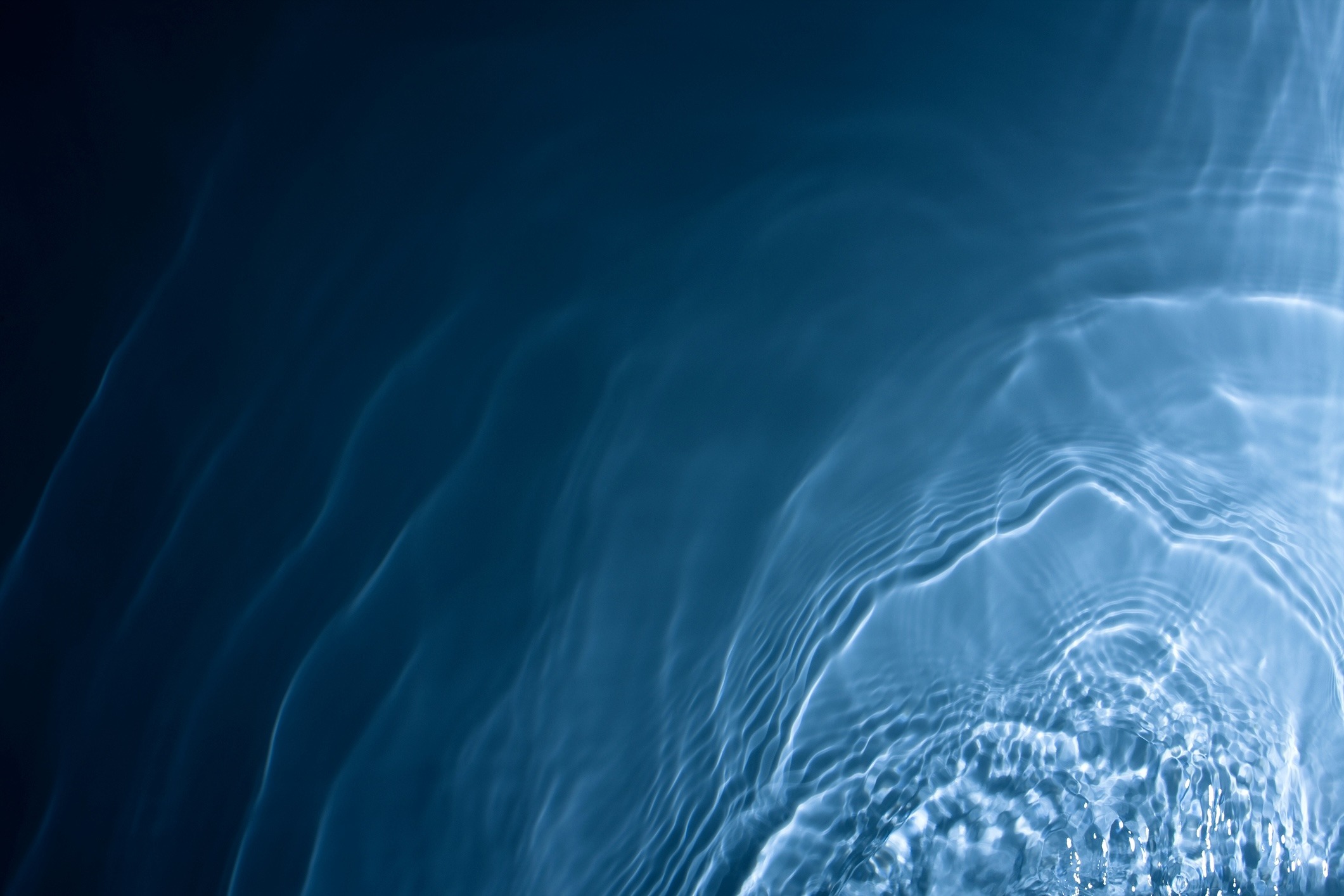 A mesmerizing view of ripples and waves in deep blue water, creating a sense of motion and tranquility with abstract reflections.