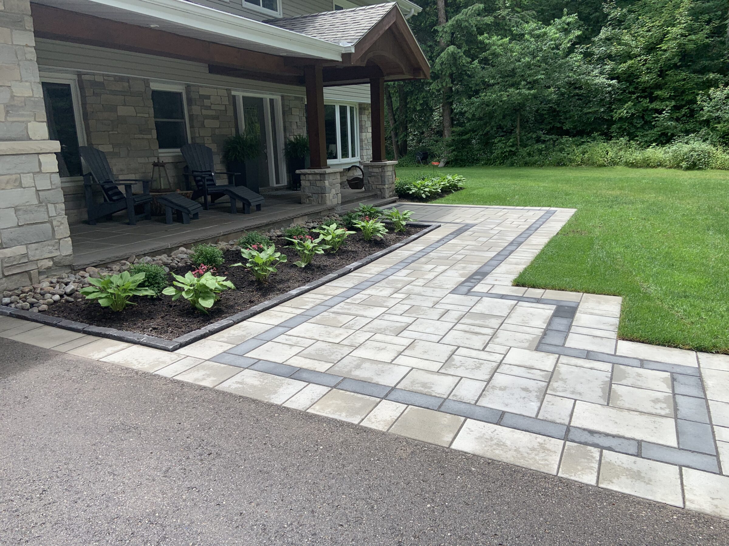A house with stone facade, front patio, and landscaped yard featuring paved walkway, bordered garden with plants, and lush green lawn.