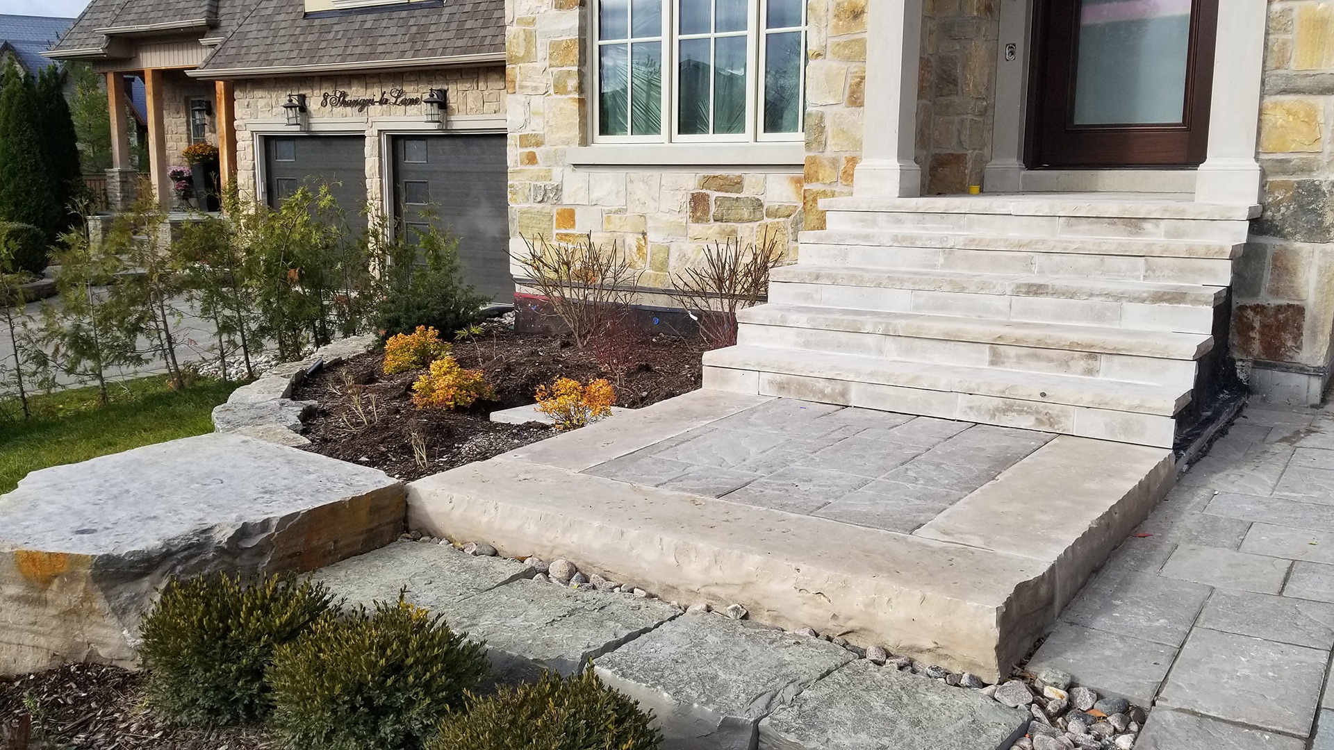 Stone steps lead to an elegant entrance of a modern house with landscaped garden and shrubs.